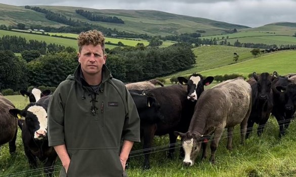 A man (Harry Sordy) stood in a field with cattle behind him facing the camera